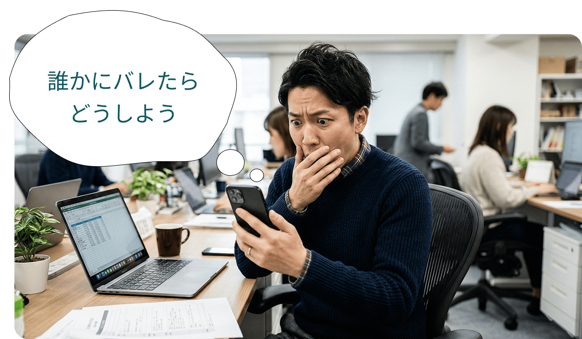 「誰かにバレたらどうしよう」と職場でスマホを見ながら不安がる男性。